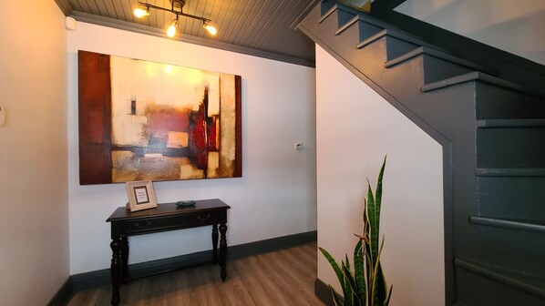 Un pasillo con un cuadro abstracto grande, un banco de madera con una placa y una escalera.