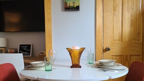 Un coin repas avec une table ronde, des chaises rouges, un centre de table composé de bougies et un tableau représentant un paysage urbain accroché au mur.