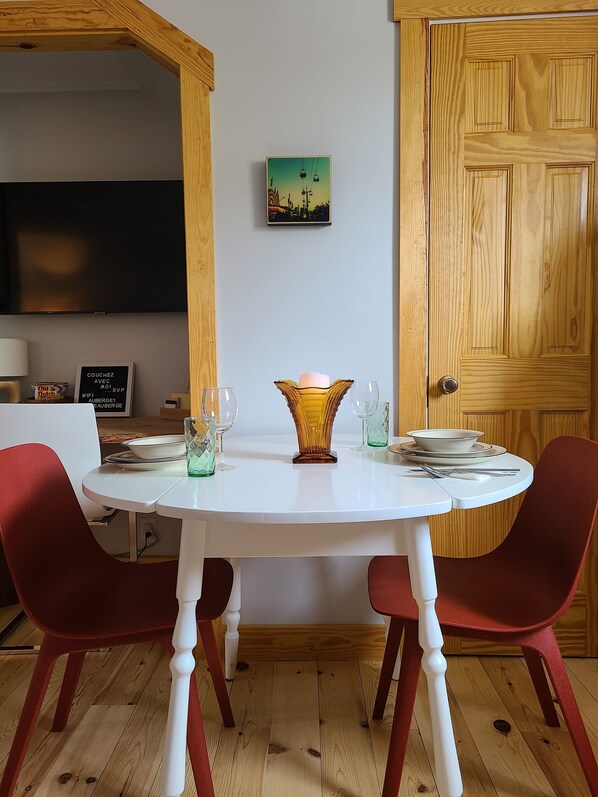 A dining area with a round table, red chairs, a candle centerpiece, and a cityscape painting on the wall. - La Petite Auberge sur Queen - Le Refuge
 (Rawdon)