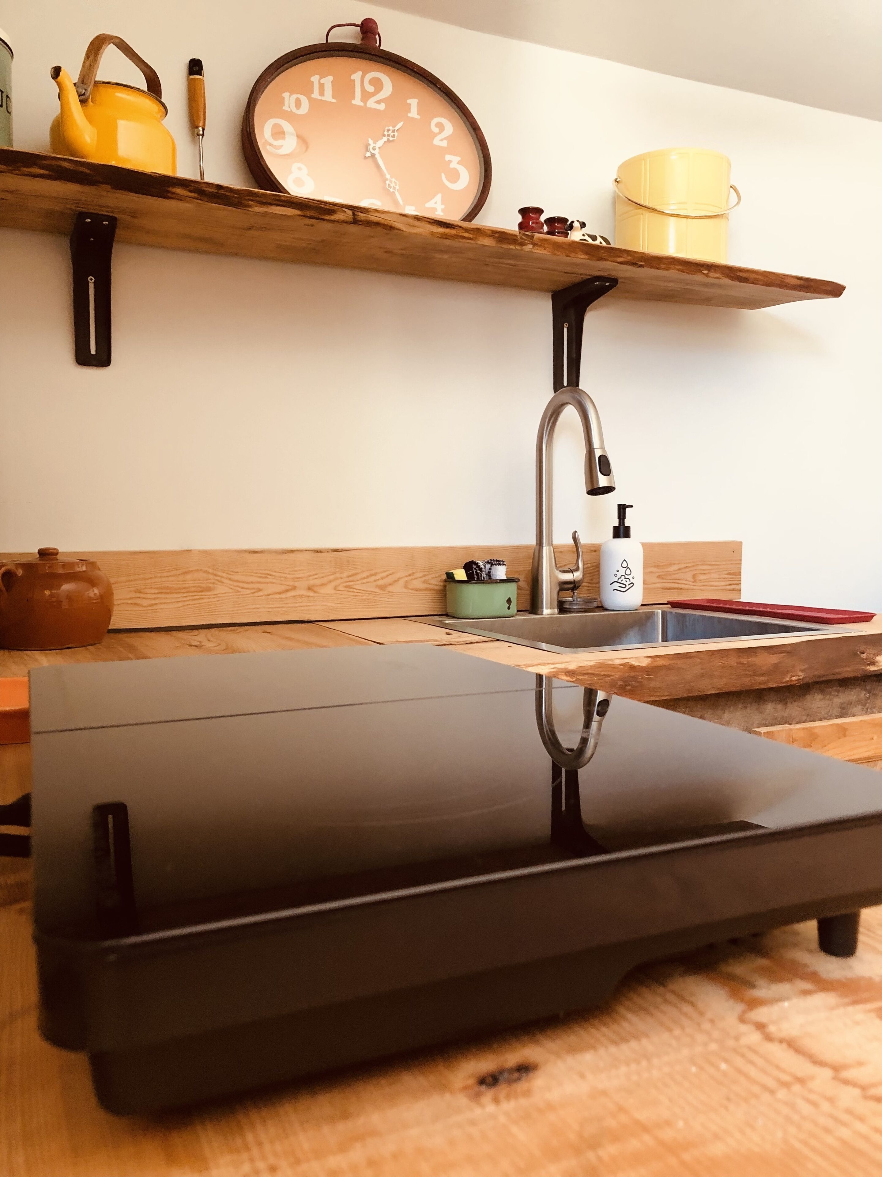 Una cocina con encimera negra, un lavamanos de acero inoxidable y estantes de madera con utensilios de cocina.