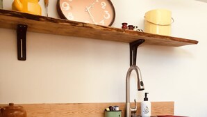 Une cuisine dotée d’un plan de travail noir, d’un évier en acier inoxydable et d’étagères en bois au-dessus, où sont rangés les ustensiles de cuisine.