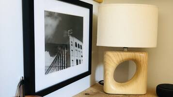 Een lijst met een zwart-witfoto aan de muur, een houten tafel met een lamp en een bruine keramische mok.