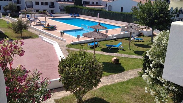 En swimmingpool omgiven av solstolar och parasoller, med utsikt över bostadshus i bakgrunden.