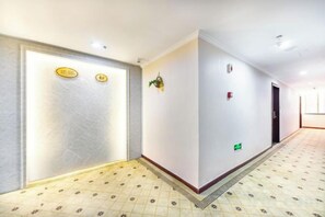 Un couloir d’hôtel avec un sol à motifs, un comptoir de réception avec une enseigne et une porte avec une plaque numérotée.