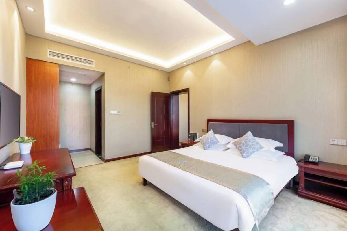 Une chambre d’hôtel avec un grand lit, une table de chevet et un petit bureau agrémenté d’une plante.