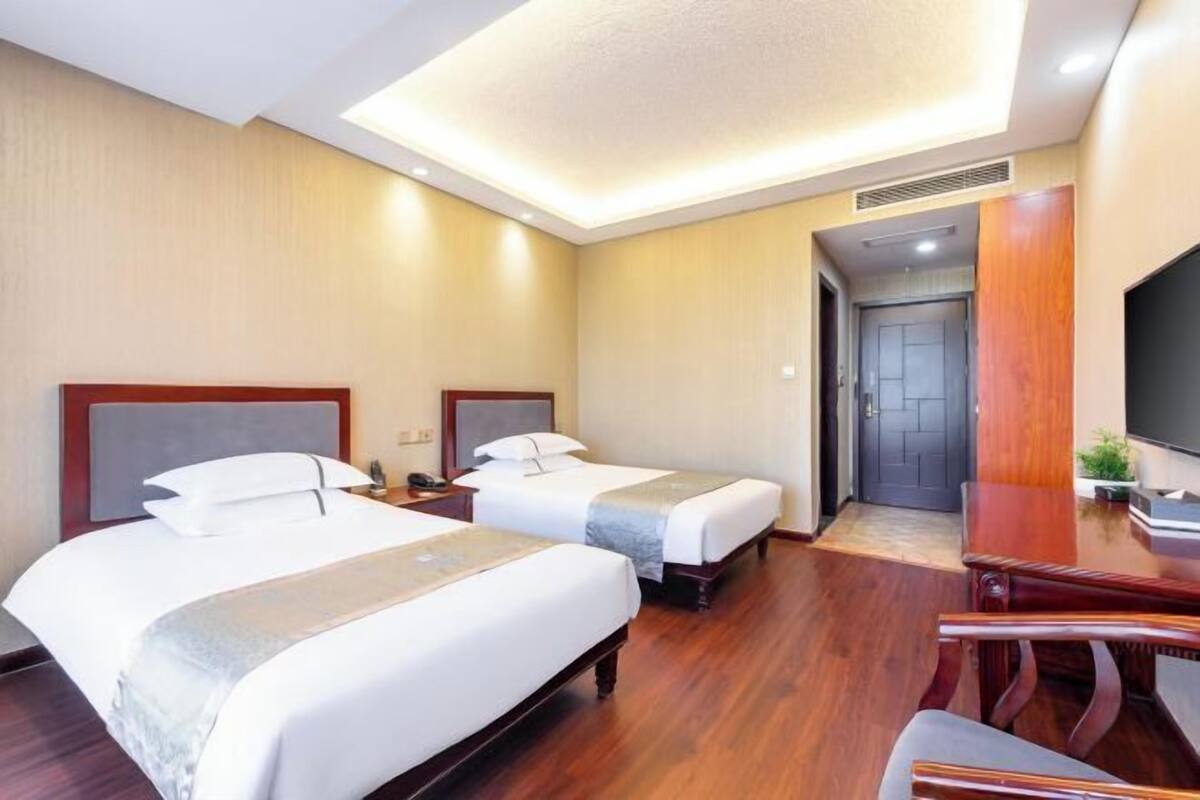 Une chambre d’hôtel avec deux lits, un bureau, une chaise et un téléviseur.
