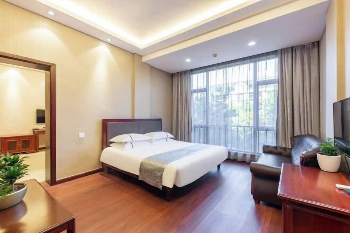 Une chambre d’hôtel avec un grand lit, un bureau, une chaise, une télévision et une fenêtre avec des rideaux.