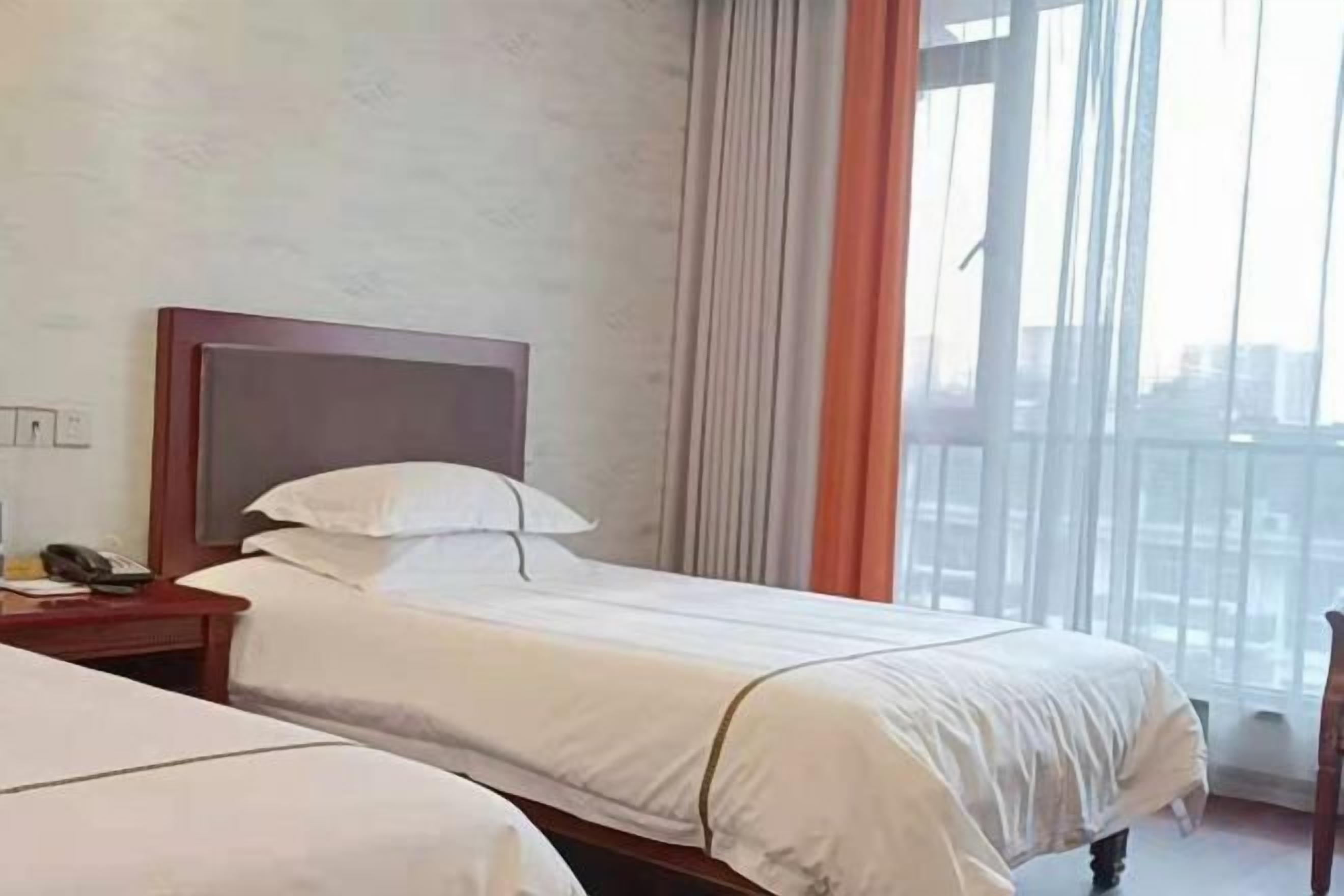 A hotel room with two beds, a nightstand, and a view of the city.