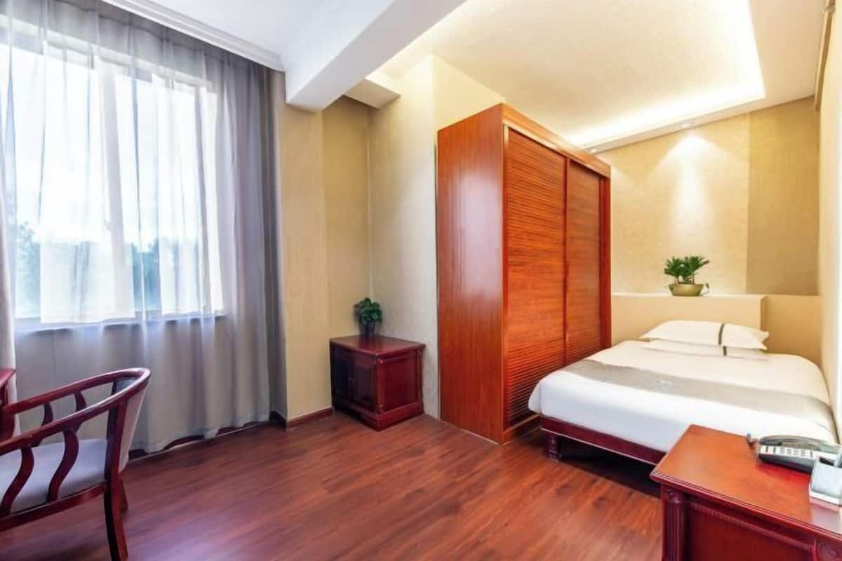 Une chambre d’hôtel comprenant un lit, un bureau, une chaise, une armoire et une fenêtre avec des rideaux.