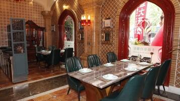 Comedor con una larga mesa dispuesta para seis, rodeada de sillas verdes, en una habitación con paredes estampadas y piso de baldosas.