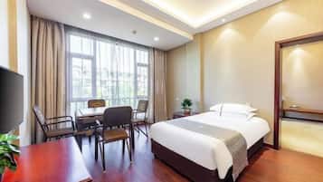 A hotel room with a bed, a desk, chairs, a TV, and a window with curtains.