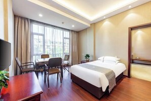 Une chambre d’hôtel avec un lit, un bureau, des chaises, une télévision et une fenêtre avec des rideaux.