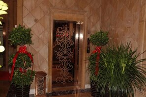 Un ascenseur doté d’une porte décorative, entouré de plantes en pot ornées de rubans rouges.