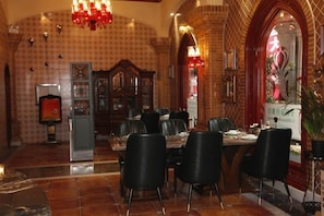 Een eetgedeelte met een hoge plafond, gewelfde bakstenen muren en een kroonluchter. Tafels zijn gedekt met stoelen.