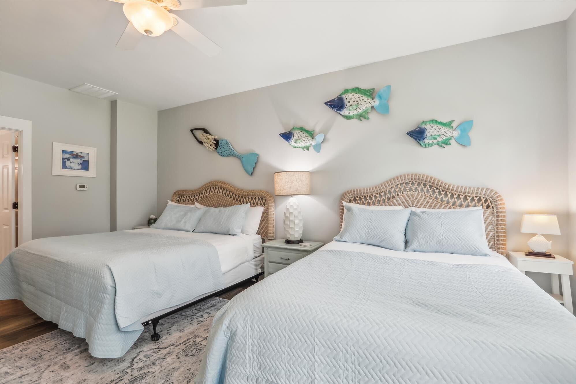 Un dormitorio con dos camas, un ventilador de techo y decoración de peces en la pared.