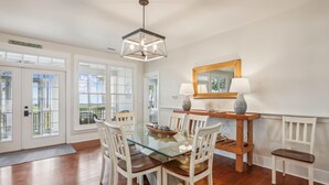 A dining area with a glass table, white chairs, a wooden sideboard, and a hanging light fixture.