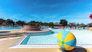 Un área de piscina con una pelota de playa grande, sillas de descanso y un cielo azul despejado.