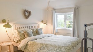 A bedroom with a white bed, two bedside lamps, a heart-shaped decoration on the wall, and a window with curtains. - 1 bedroom accommodation in Sway, near Lymington (Sway, near Lymington)