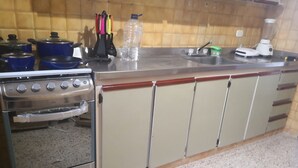 Uma cozinha com fogão de aço inoxidável, forno embutido, pia e bancada com diversos itens, incluindo uma garrafa de água e um liquidificador.