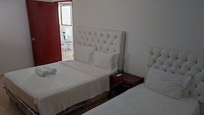Quarto com duas camas, uma mesa de cabeceira de madeira e uma porta vermelha.