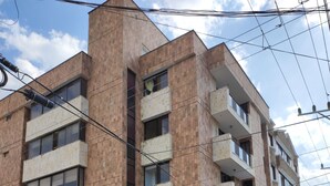Um edifício de vários andares com fachada de tijolos, varandas e um táxi amarelo estacionado na frente.
