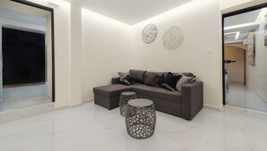 Een moderne woonkamer met een grijze hoekbank, twee bijzettafeltjes met een patroon en abstracte muurkunst.