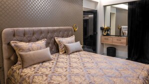 Een slaapkamer met een knopen hoofdbord, een groot bed met beddengoed met een patroon, een spiegel en een kaptafel met een zwart gordijn.