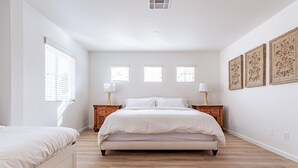 Un dormitorio espacioso con una cama grande, dos mesitas de noche y tres ventanas.