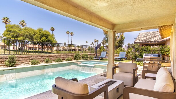 Un área de piscina con sillones de descanso, una parrilla y vistas a palmeras y un edificio.