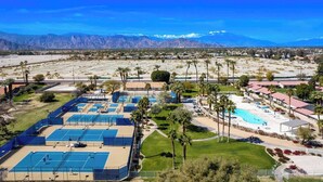 Vista aérea de un resort con múltiples canchas de tenis, una piscina y un telón de fondo montañoso.