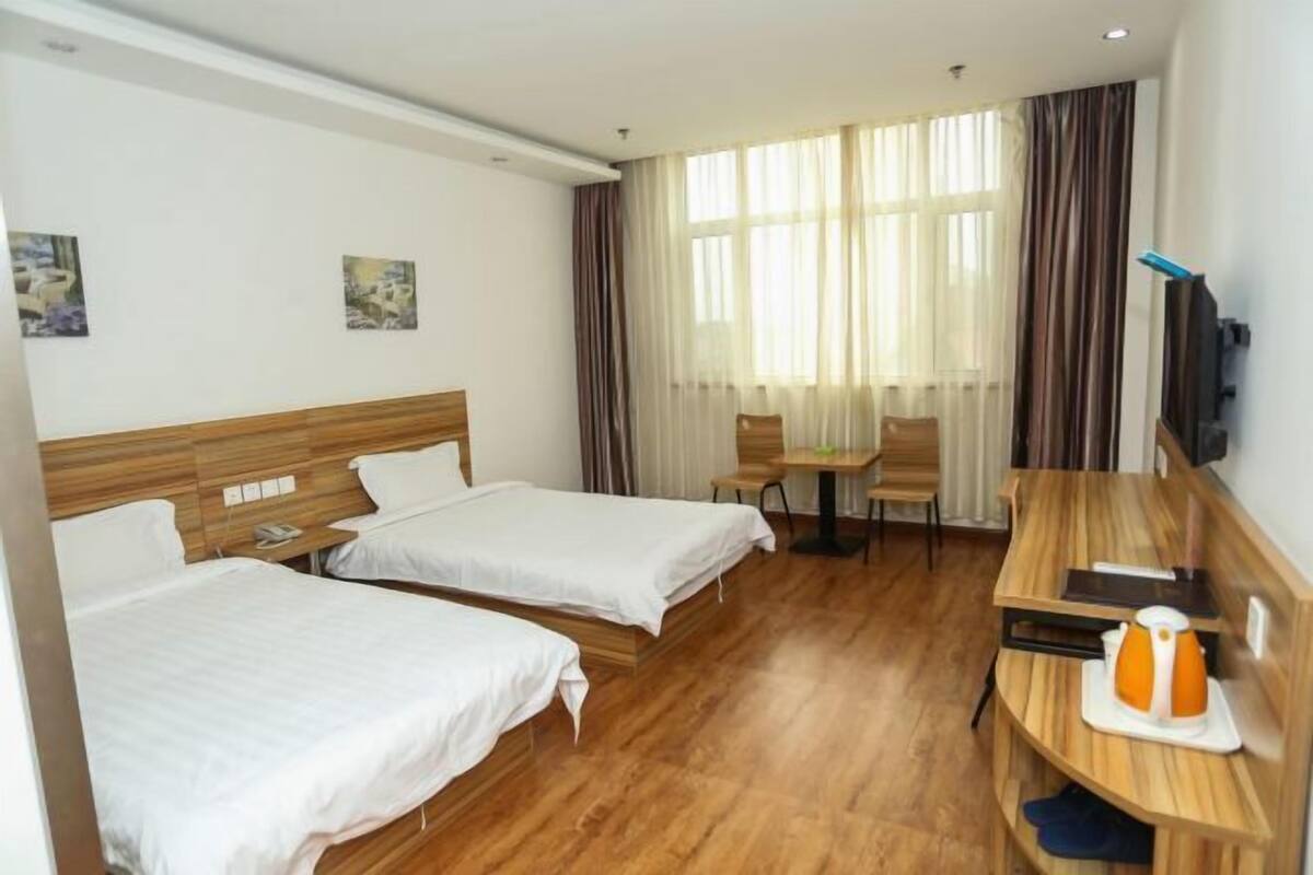A hotel room with two beds, a desk, a chair, a television, and a window with curtains.