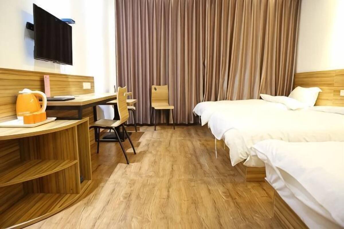 A hotel room with a wooden desk, a chair, a bed, and a TV mounted on the wall.