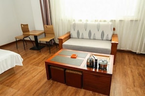 A room with a bed, a sofa, a wooden coffee table with a kettle and a cup, and a chair.