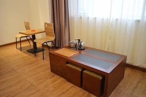 Una habitación con una mesa de comedor de madera y sillas, una pequeña cocina con hervidor y una ventana con cortinas.