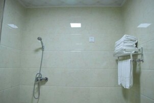 Un área de ducha con cabezal de ducha de mano, un perchero con toallas dobladas e interruptor de luz en la pared.