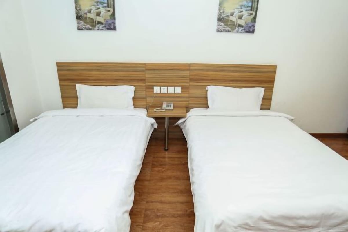 A hotel room with two single beds, a wooden headboard, a bedside table with a phone, and two wall-mounted paintings.