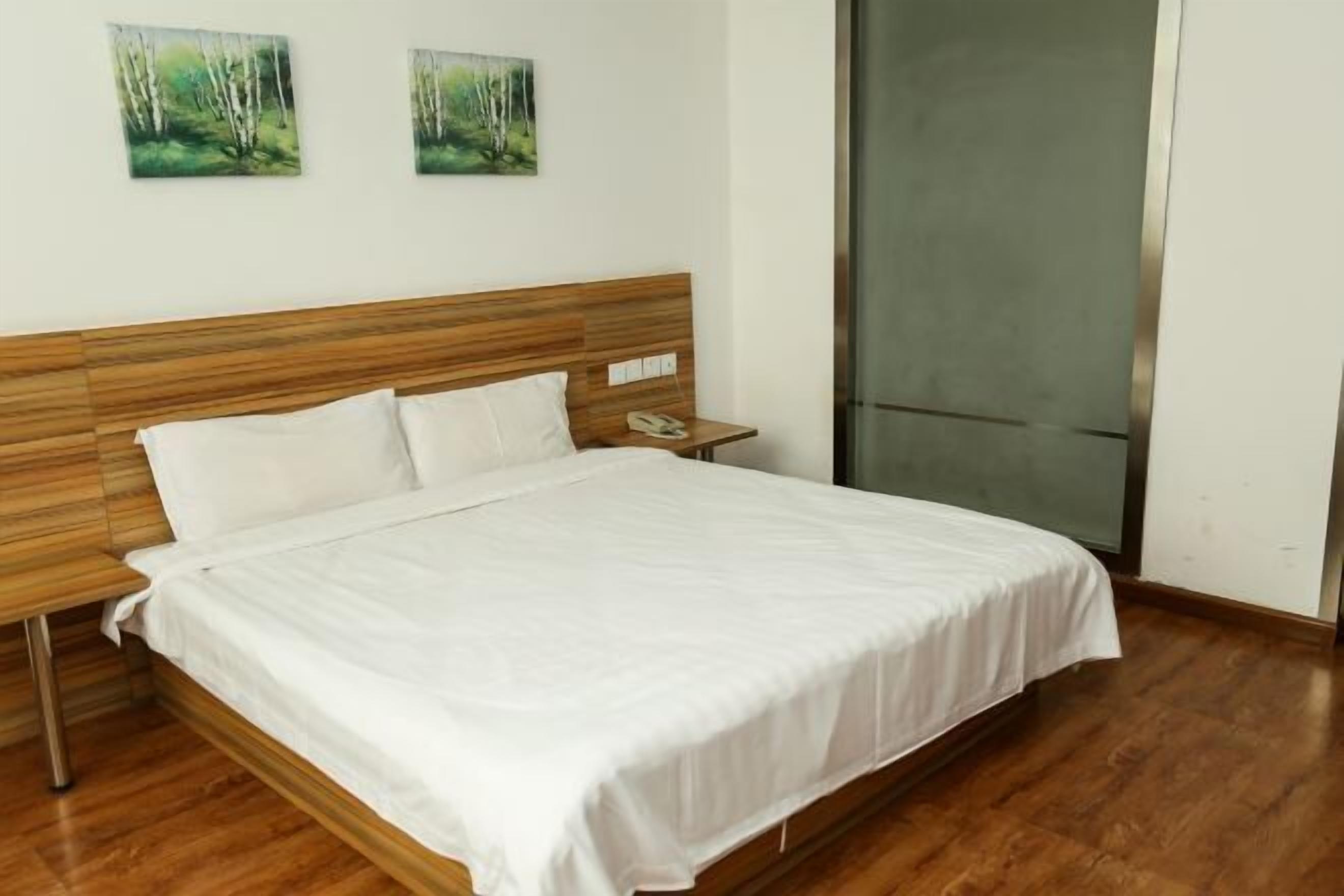 Een net opgemaakt bed met witte lakens, een houten hoofdbord en een nachtkastje met een telefoon.