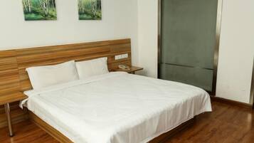 Een net opgemaakt bed met witte lakens, een houten hoofdbord en een nachtkastje met een telefoon.