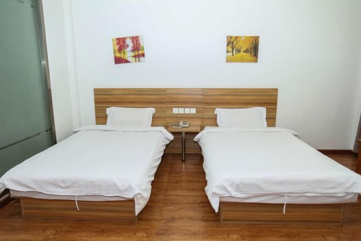 A double room with two beds, wooden headboard, white bedding, and two wall-mounted paintings.