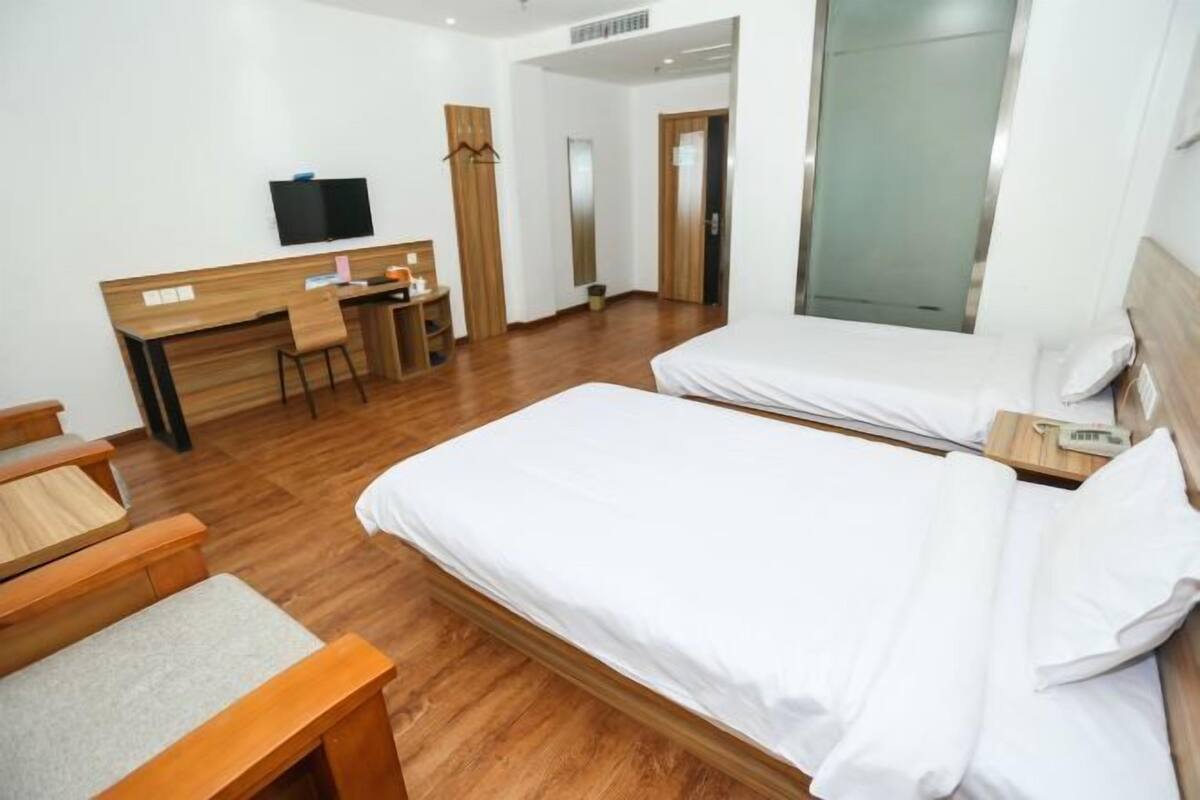 A hotel room with two beds, a desk, a chair, a television, and a mirror.