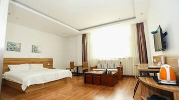 Una habitación de hotel con una cama de madera, un escritorio con una silla, una mesita de centro, un televisor montado en la pared y una ventana con cortinas.