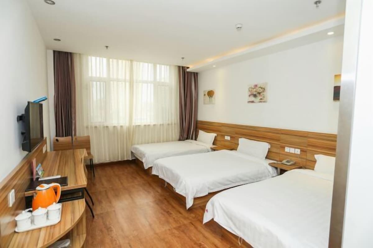 A hotel room with two beds, a wooden desk with a coffee maker, a TV, and a window with curtains.