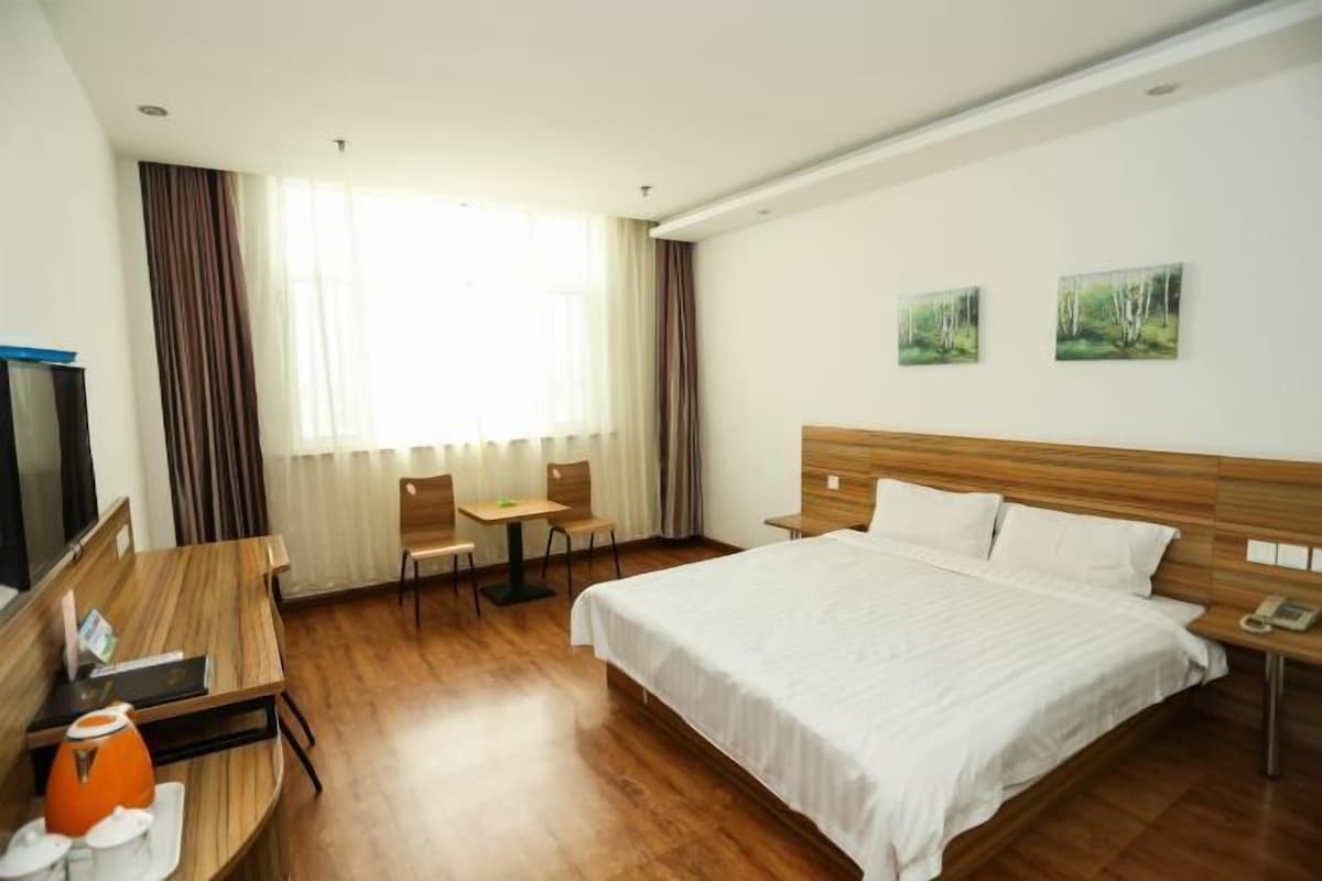 A hotel room with a wooden bed, a desk with a chair, a small table, and a TV.