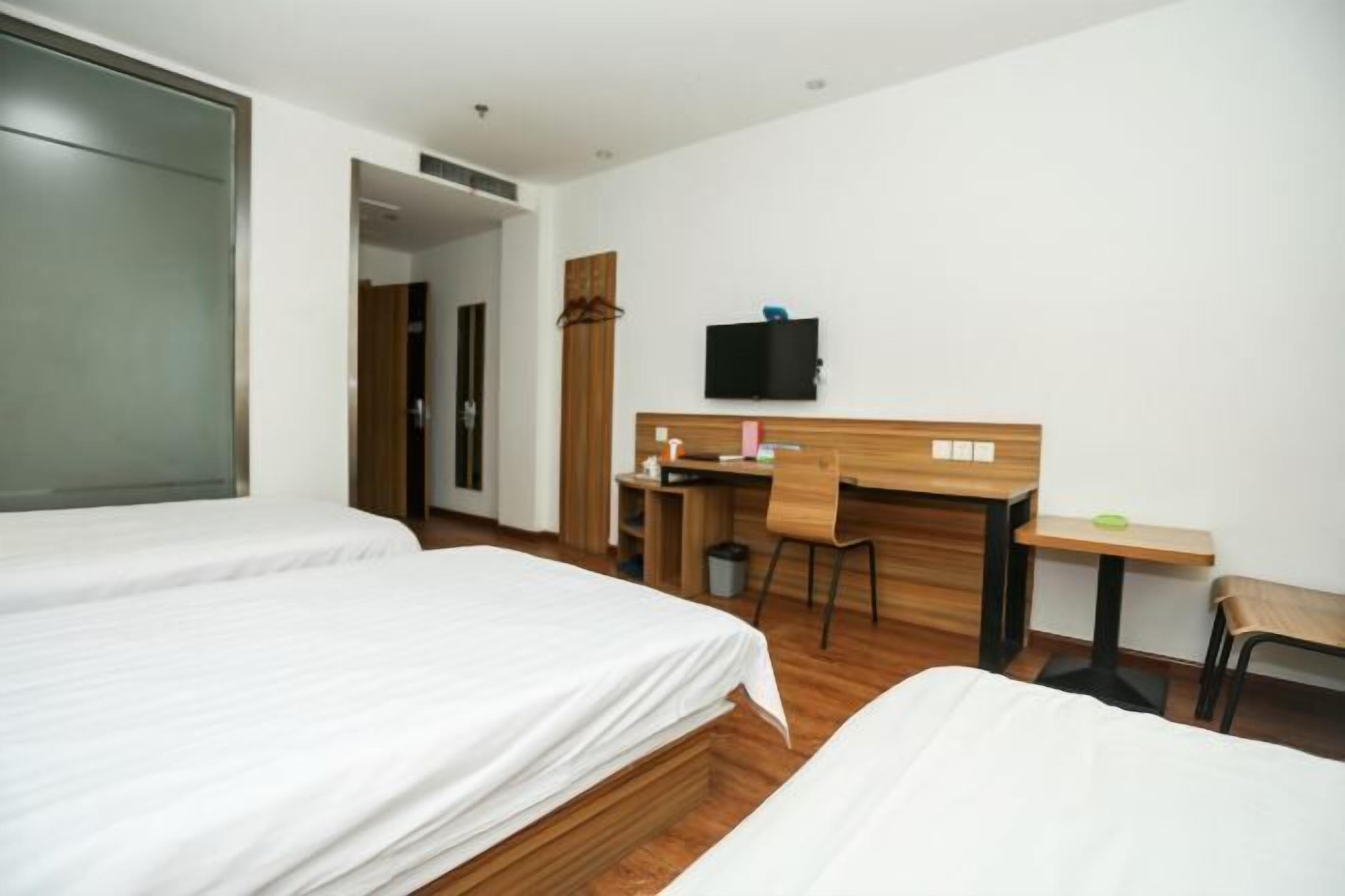 A hotel room with two beds, a desk, a chair, a television, and a small table.