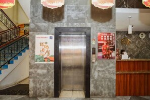 An elevator, a reception desk, a staircase, and a wall with a poster. - Shangjia Hotel (Anping)