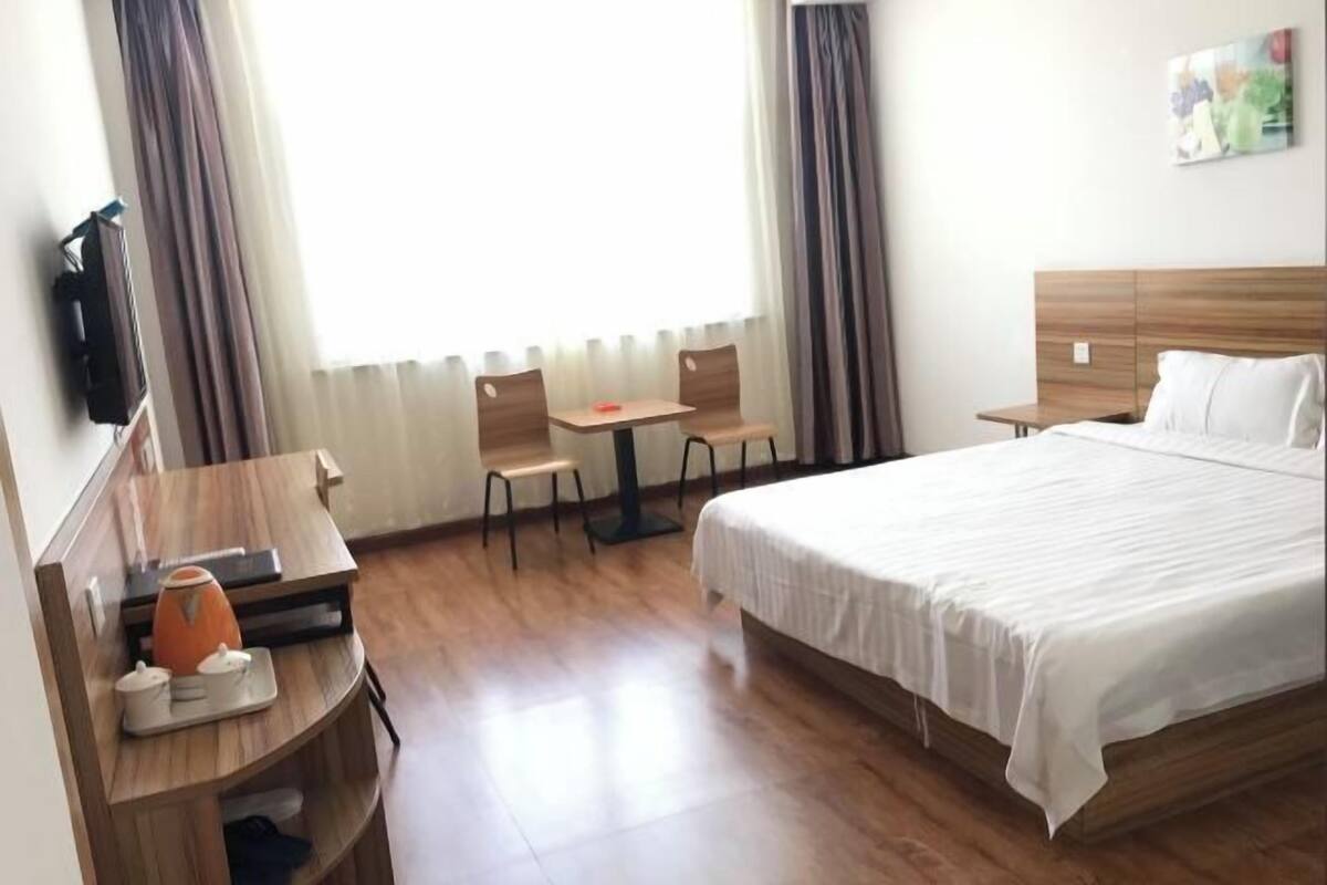 A hotel room with a bed, a desk with a chair, a small table, and a television.