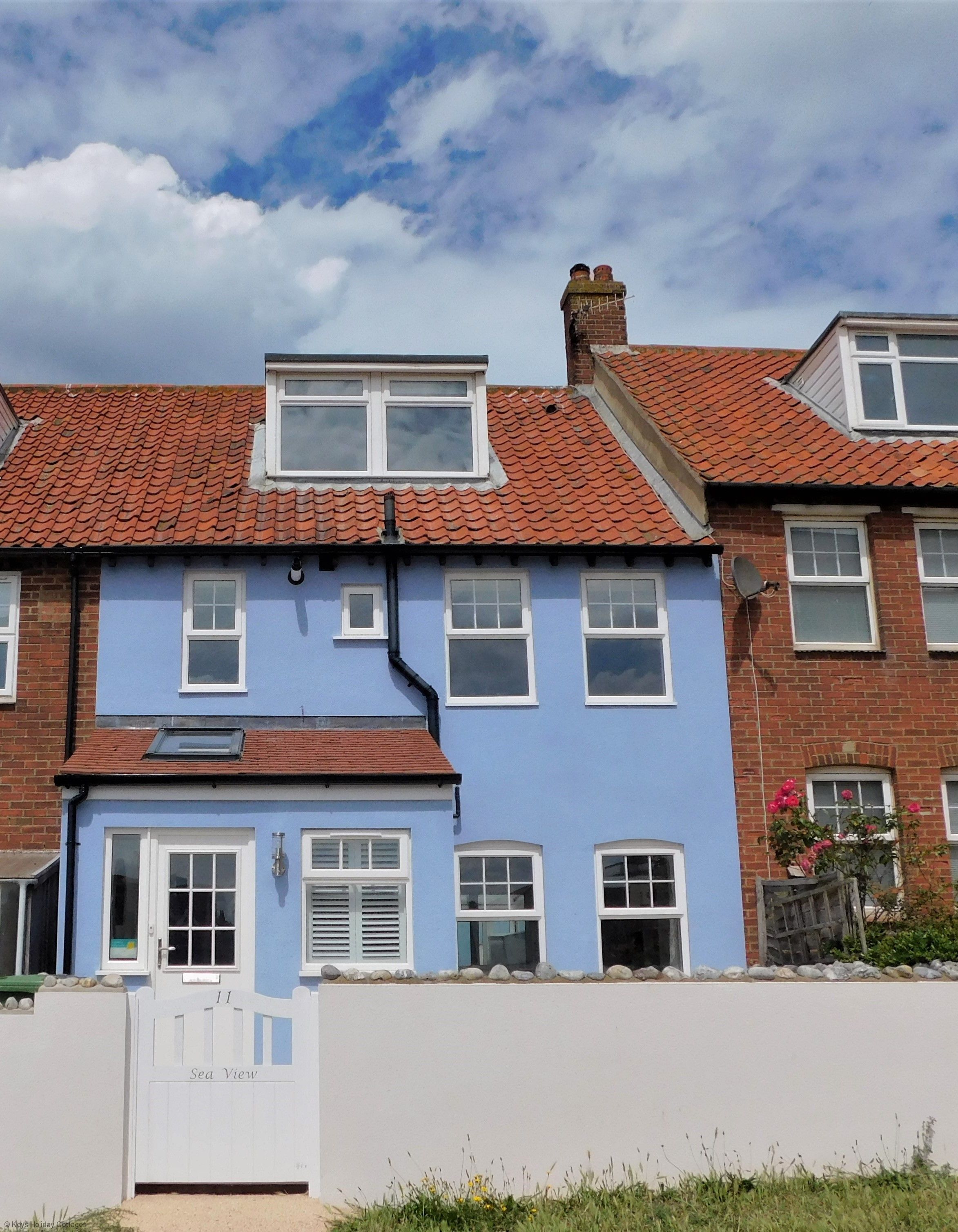 A two-story house with a red-tiled roof, a blue facade, and a white gate labeled "Sea View".