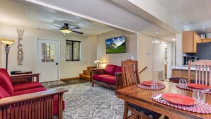 A spacious living area with a wooden dining table set for four, a red sofa, and a television mounted on the wall. - Family-Friendly Forest Cabin-Sleeps 20-3 Levels of Fun w/ Arcade & Pool Table (arnold)