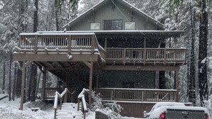 A two-story cabin with a balcony, surrounded by snow-covered trees. - Family-Friendly Forest Cabin-Sleeps 20-3 Levels of Fun w/ Arcade & Pool Table (arnold)