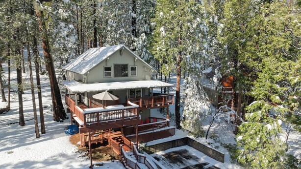 A two-story cabin with a balcony and a covered patio area, surrounded by snow-covered trees. - Family-Friendly Forest Cabin-Sleeps 20-3 Levels of Fun w/ Arcade & Pool Table (arnold)